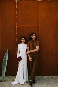 a man and woman standing next to each other in front of a rusted wall