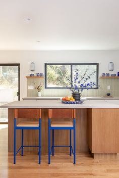 a kitchen with two blue stools next to a center island and an open window