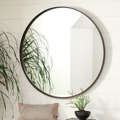 a round mirror hanging on the wall next to a table with a pillow and potted plant