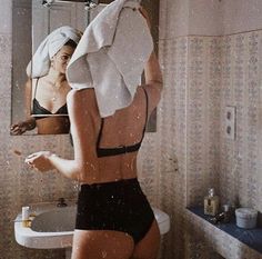 a woman standing in front of a mirror brushing her teeth with a towel over her head