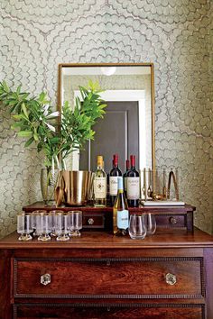 a wooden dresser topped with lots of bottles and glasses next to a mirror on top of it