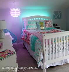 a white bed sitting in a bedroom next to a purple wall and a green light