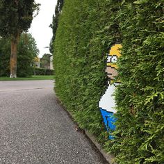 a hedge with a lego face on it is next to a sidewalk and street in front of a house