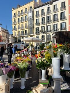 many different types of flowers are on display in front of buildings and people walking by