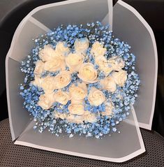 a bouquet of white roses and blue baby's breath in a clear plastic box