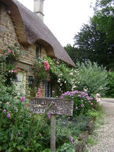 an old stone house with flowers growing on the side and a street sign in front