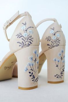 a pair of white high heels with blue flowers painted on the upper part of each shoe