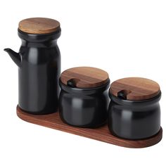 three black ceramic containers with wooden lids on a wood tray, set against a white background