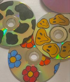 three cds with different designs on them are sitting next to each other and one has a smiley face painted on it
