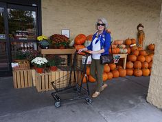a woman standing next to a shopping cart filled with pumpkins