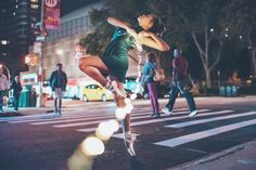 a person jumping in the air on a city street at night with people walking around