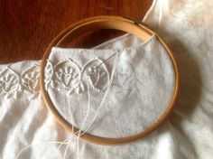 a wooden hoop with some white thread in it on a table next to a piece of cloth