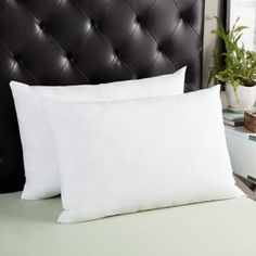 two white pillows sitting on top of a bed next to a black leather headboard
