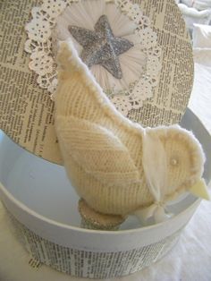 a knitted bird sitting on top of a white container next to a doily