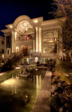 a large house with a fountain in front of it at night time, lit up by lights