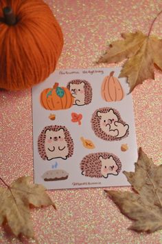 an orange pumpkin and some stickers on a pink surface with leaves, yarn and acorns