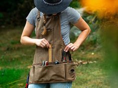 a woman wearing an apron and hat with tools in her pocket while standing outside on the grass