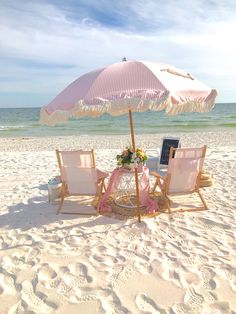 two beach chairs and an umbrella on the sand at the beach with flowers in vases