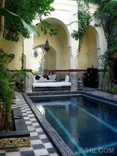 an indoor swimming pool surrounded by greenery and tiled flooring, with seating area in the middle