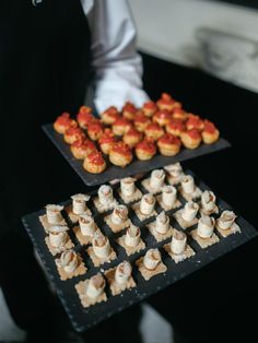 two trays filled with small pastries on top of a black table next to each other