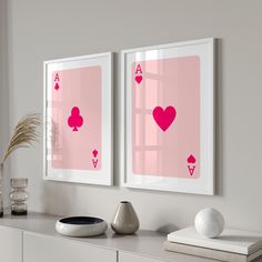two framed pictures with pink playing cards on the wall next to a vase and potted plant