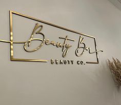 the logo for beauty box is gold and black on a white wall with dried flowers
