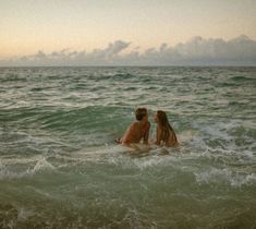 two people sitting in the ocean with one holding his head out to kiss while the other looks at him