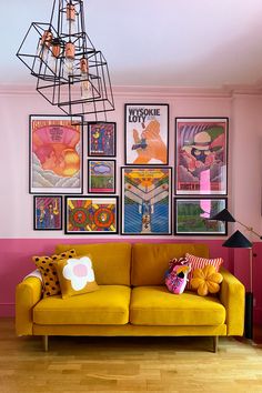 a yellow couch sitting in front of a pink wall with posters on it's walls