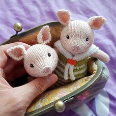 two small knitted animals in a purse on a purple cloth covered bed with a person's hand