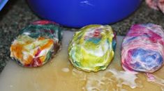 four rolls of colorful fabric sitting on top of a cutting board next to a blue bowl