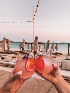 two people holding up glasses with drinks on the beach