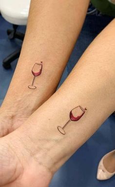 two people with matching tattoos on their arms holding wine glasses and one has a red wine glass in the other hand