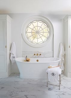 the bathroom is white and has an oval window above it, along with a claw foot tub