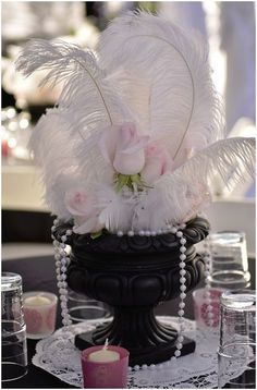 an image of a vase with flowers and feathers in it on a table next to candles