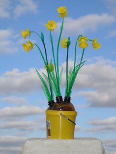 some yellow flowers are sitting in a brown vase on a table with blue sky and clouds behind them
