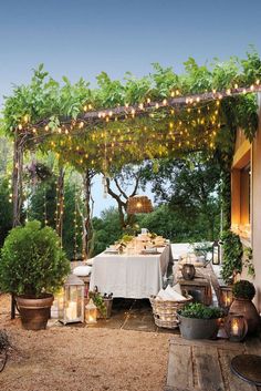 an outdoor dining area with potted plants and lights strung from the pergolated arbor