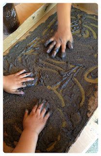 two children are playing with mud on the floor and one child is reaching for something