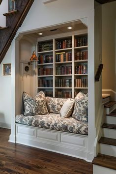 a couch sitting in front of a bookshelf filled with lots of books next to a stair case