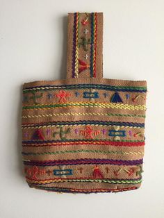 a woven bag hanging on the wall with colorful trimmings and beads around it