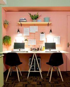 two laptops are sitting on a desk in front of a wall with pink tiles