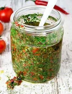 a jar filled with green stuff next to tomatoes
