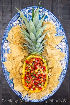 a pineapple with salsa and chips on a blue and white plate next to a wooden table