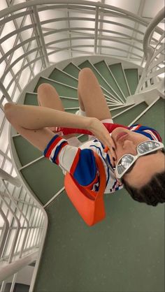 a woman laying on the ground in front of a spiral stair case holding an orange purse