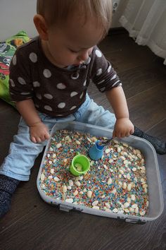 a toddler sitting on the floor playing with a tray of sprinkles
