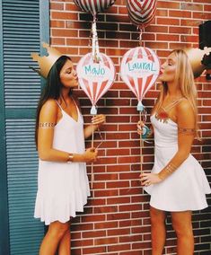 two beautiful young women standing next to each other in front of a brick wall with balloons