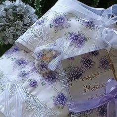 an open book with purple flowers and ribbon on it next to a bouquet of flowers