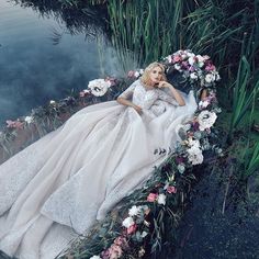 a woman laying on top of a lush green field next to water wearing a wedding dress