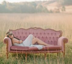 a woman laying on top of a pink couch in a field