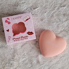 a pink heart shaped soap next to a box of lipstick on a white carpet with the lid open