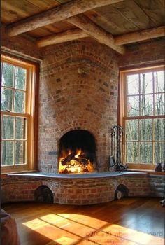 a brick fireplace in the corner of a room with two large windows and wood flooring